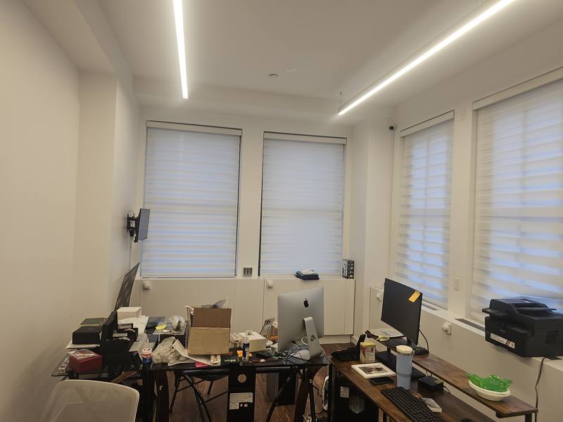 Corner of an office with zebra shades on two window walls above workstations